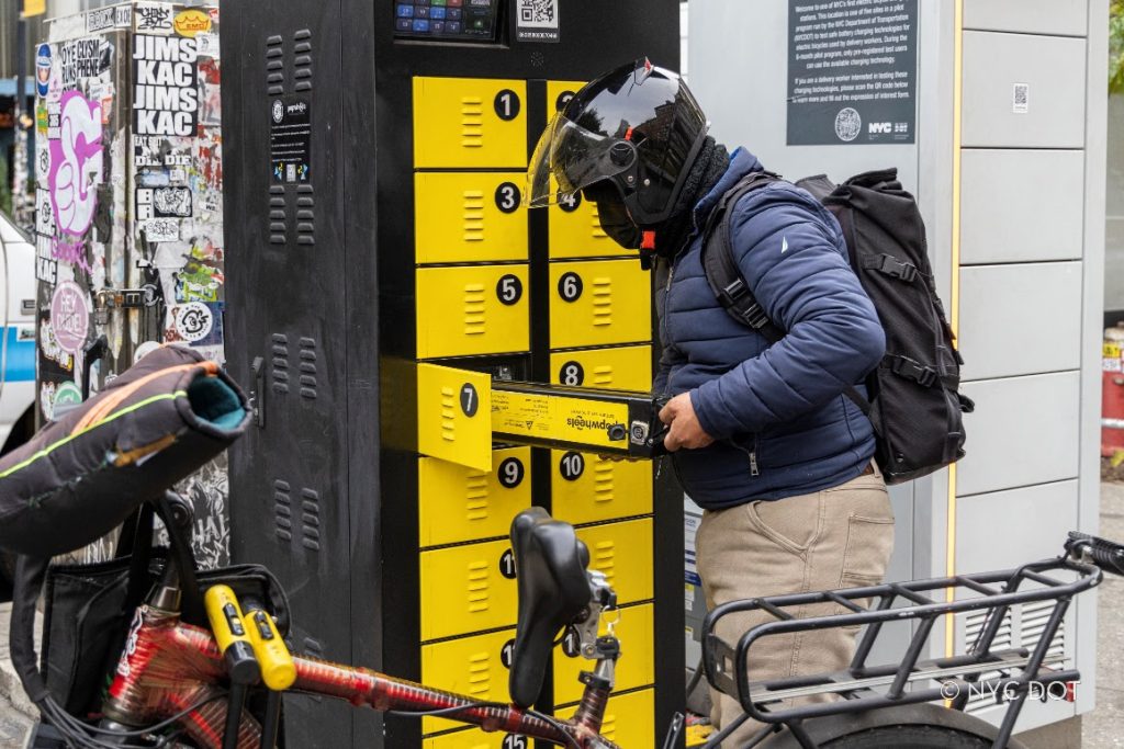 Un repartidor cambia las baterías de una bicicleta eléctrica utilizando un armario de intercambio de baterías implementado a modo de prueba en 2024. Crédito: NYC DOT
 
