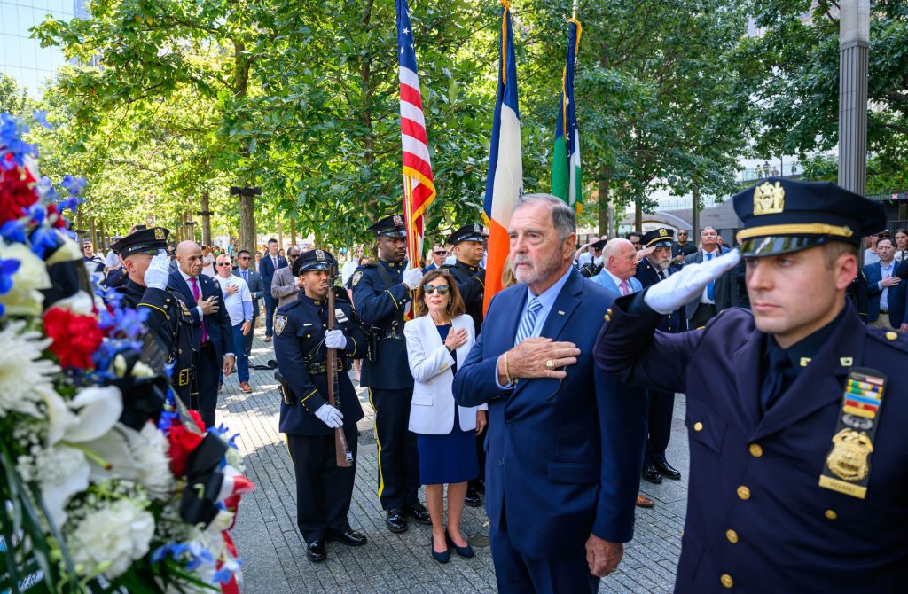 Acto conmemorativo en Nueva York con agentes de la Policía de Nueva York, banderas y una ofrenda floral en homenaje a las víctimas del 11-S.